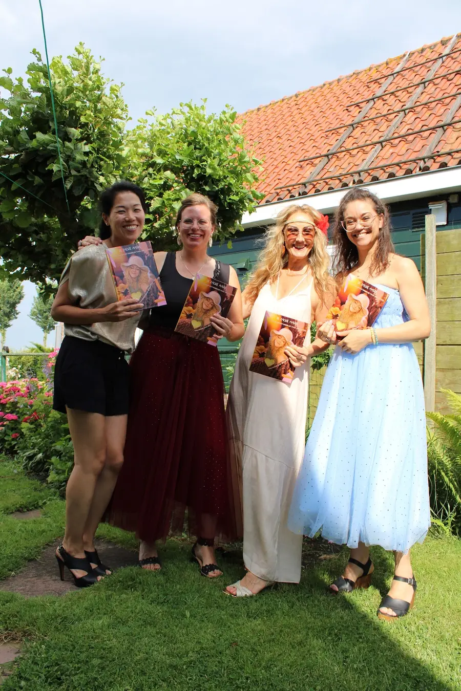 Vier vrouwen houden in een zonnige tuin het boek Zachte Aarde omhoog