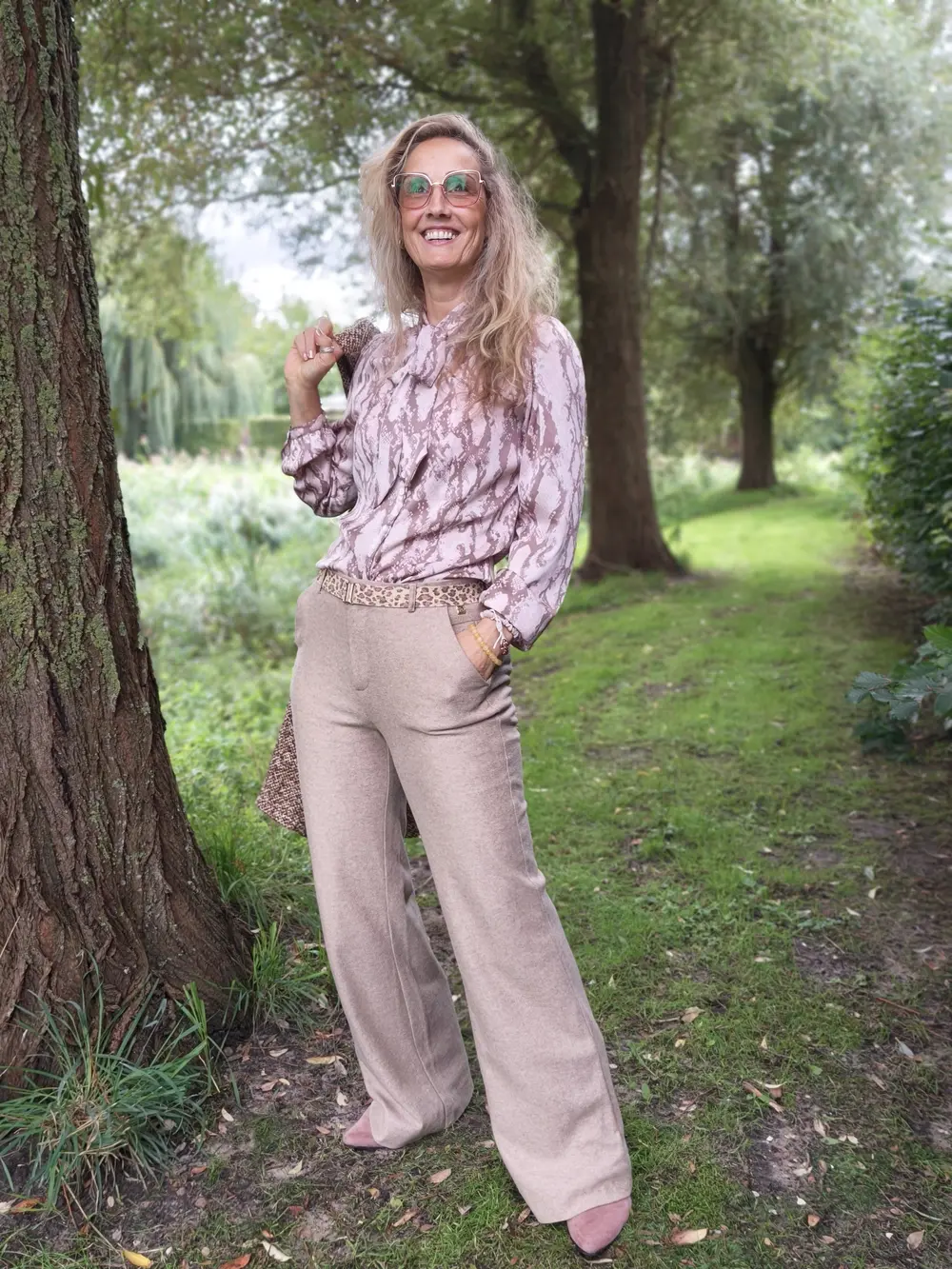 DjezzManon lachend in het park, in een roze blouse en zandkleurige broek