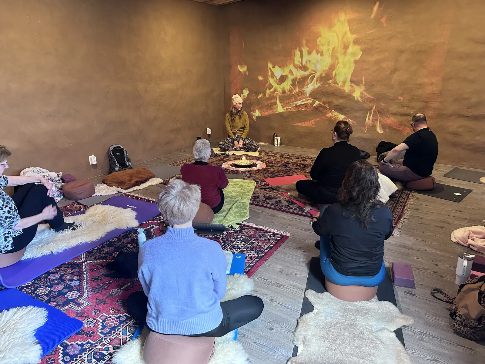 Een groep vrouwen zit op kussens in meditatie bij een warm haardvuur tijdens een event van DjezzManon